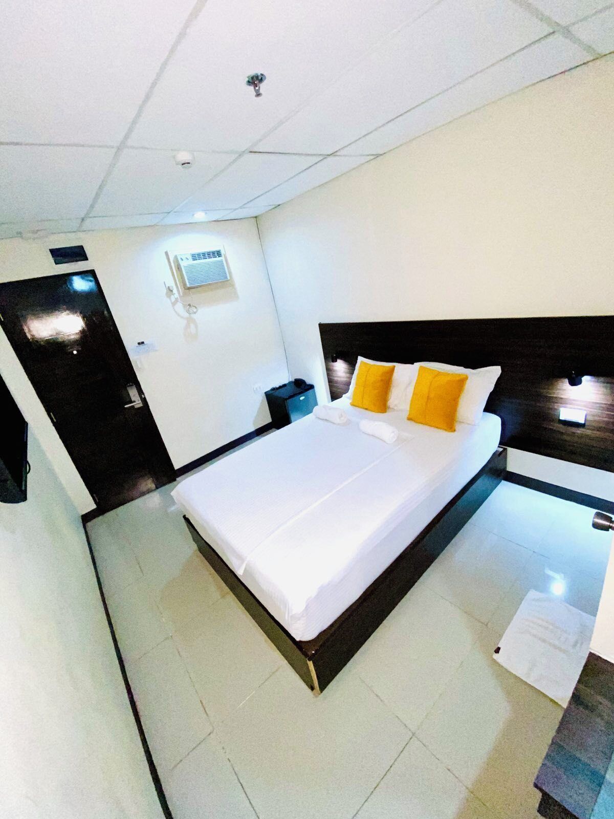 A modern hotel room with a large bed, a nightstand, a desk, and a wall-mounted air conditioning unit.