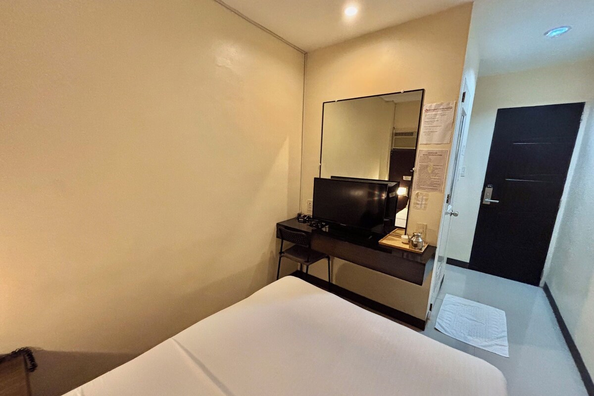 A hotel room with a bed, a desk with a computer, a mirror, and a door.