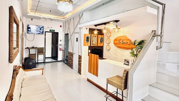 A reception area with a reception desk, a bench, a staircase, and a wall-mounted clock. - Anton's Inn Hotel (Balanga)