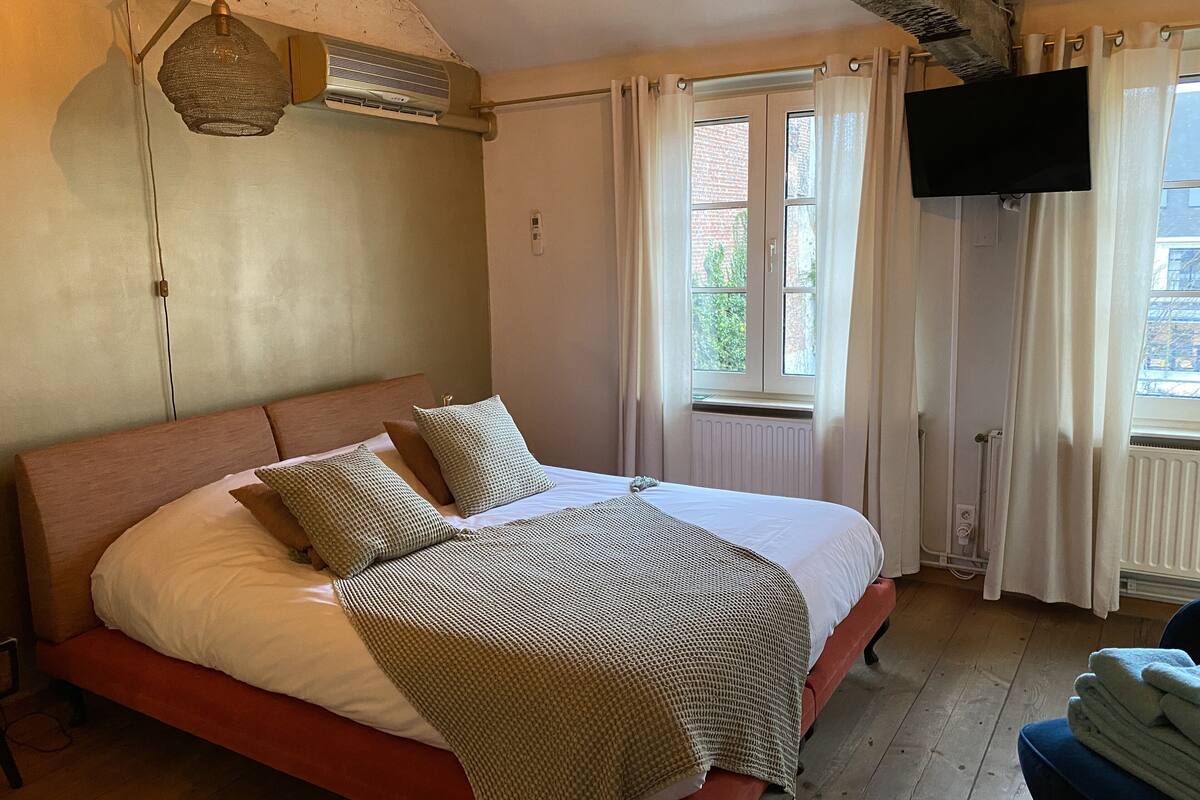 A bedroom with a bed, a television, a window with curtains, and an air conditioning unit.