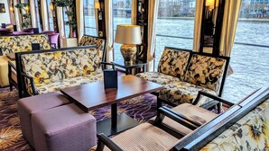 A luxurious interior with floral upholstery sofas, a wooden coffee table, and a view of a river. - Select MS Charles Dickens - Cologne (Cologne)