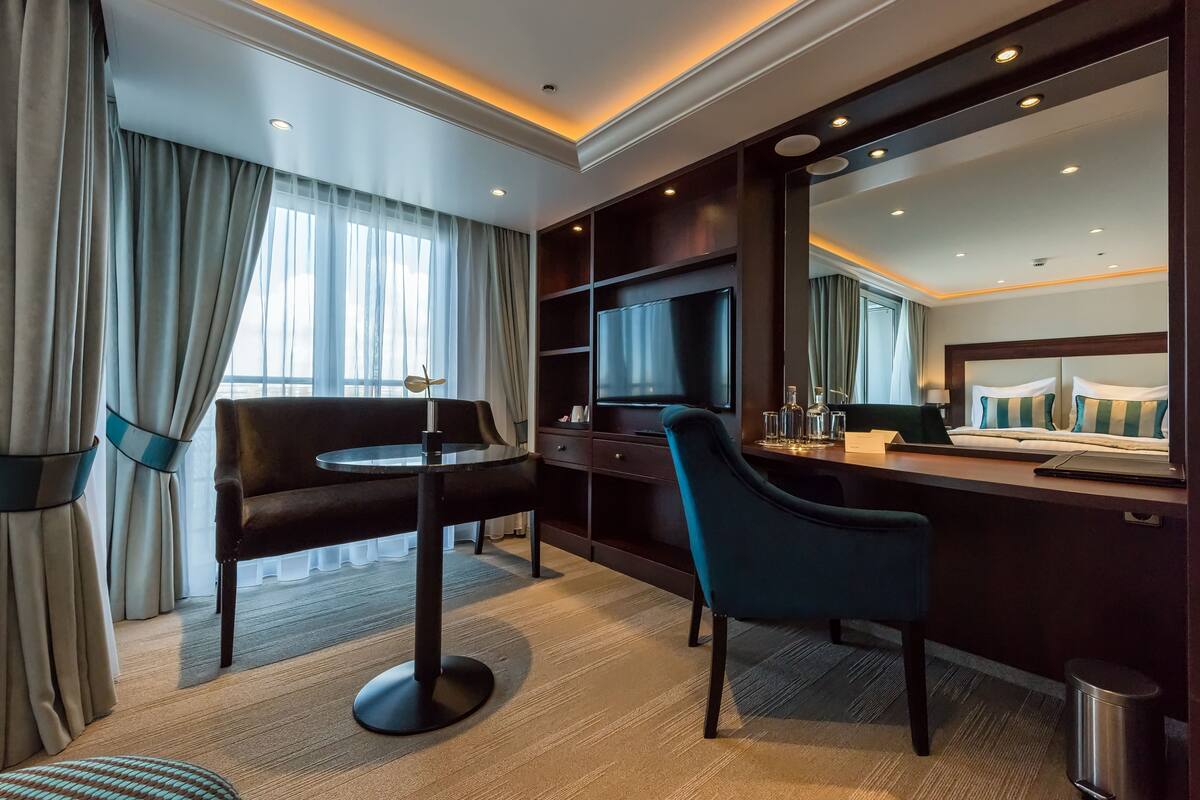 Une chambre d’hôtel avec un bureau en bois foncé, un téléviseur fixé au mur, un canapé confortable et une petite table ronde.