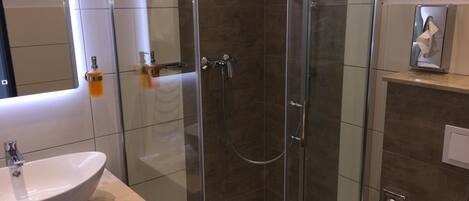 Une salle de bain moderne avec une douche à parois de verre, un lavabo rond et un miroir au-dessus du lavabo.