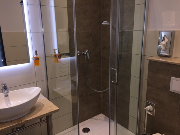 Un baño moderno con ducha de vidrio, un lavamanos redondo y un espejo sobre el lavabo.