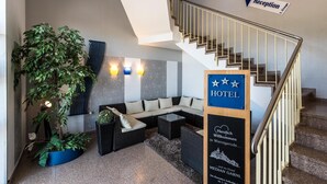 A hotel reception area with a staircase, a sofa set, and a potted plant. - Median Hotel Garni (Wernigerode)