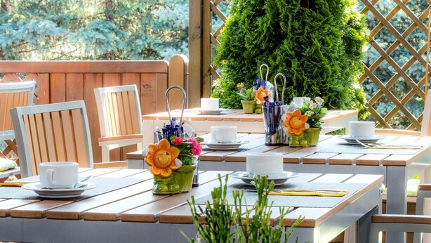 An outdoor patio with wooden tables and chairs, some with cups and saucers, and flower arrangements. - Median Hotel Garni (Wernigerode)