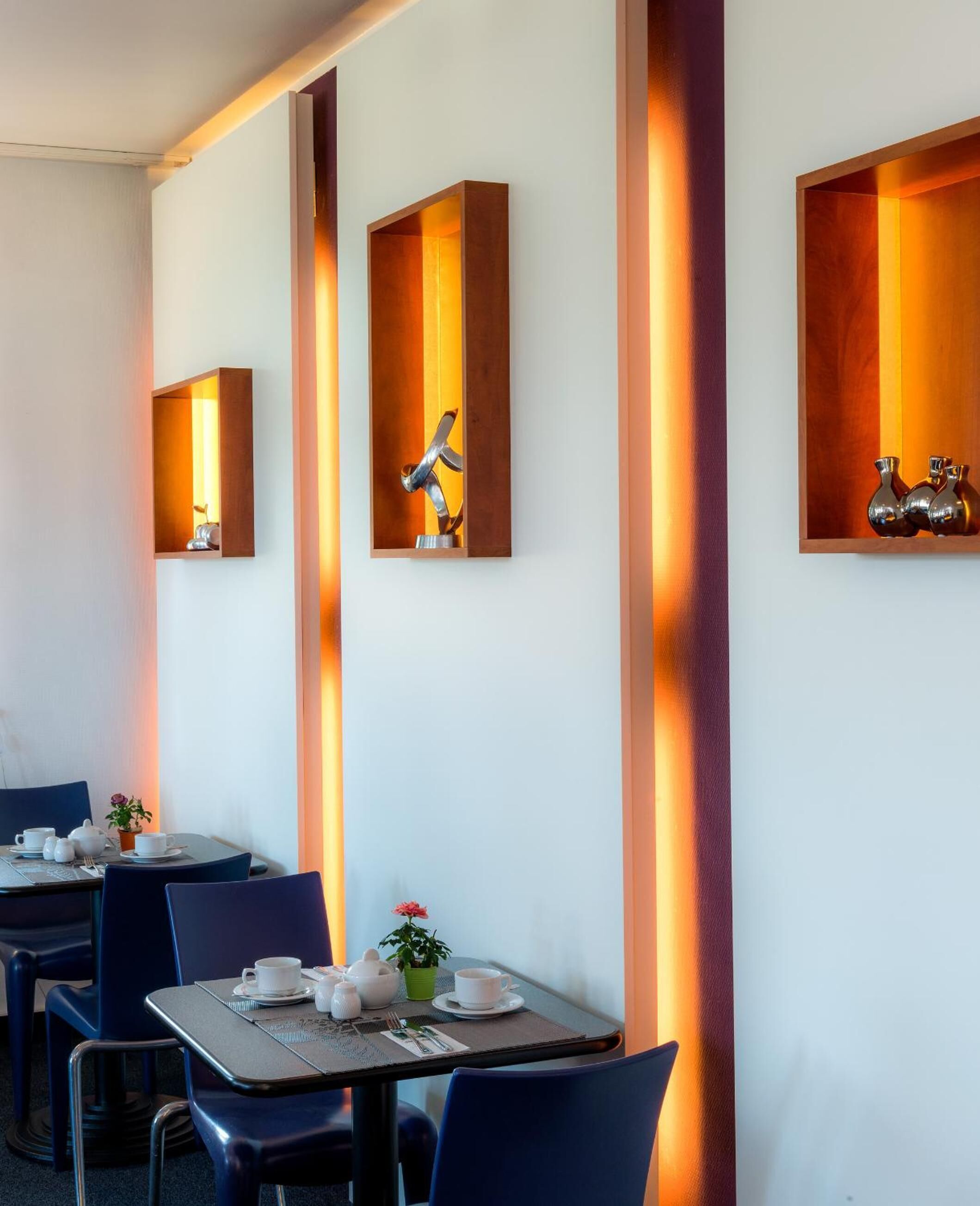 A modern dining area with tables and chairs, decorative wall sconces, and a minimalist decor style.