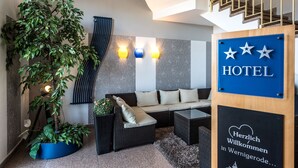A hotel lobby with a sofa, a coffee table, a large potted plant, and a sign indicating the hotel's name. - Median Hotel Garni (Wernigerode)