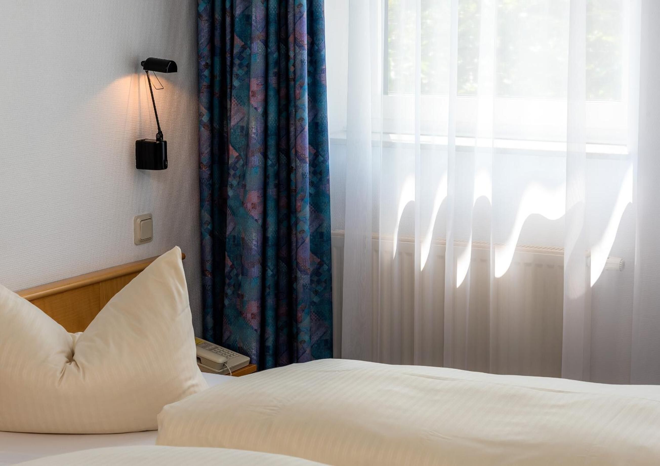 Ein Hotelzimmer mit einem Bett, einer Nachttischlampe, einem Telefon und Vorhängen.