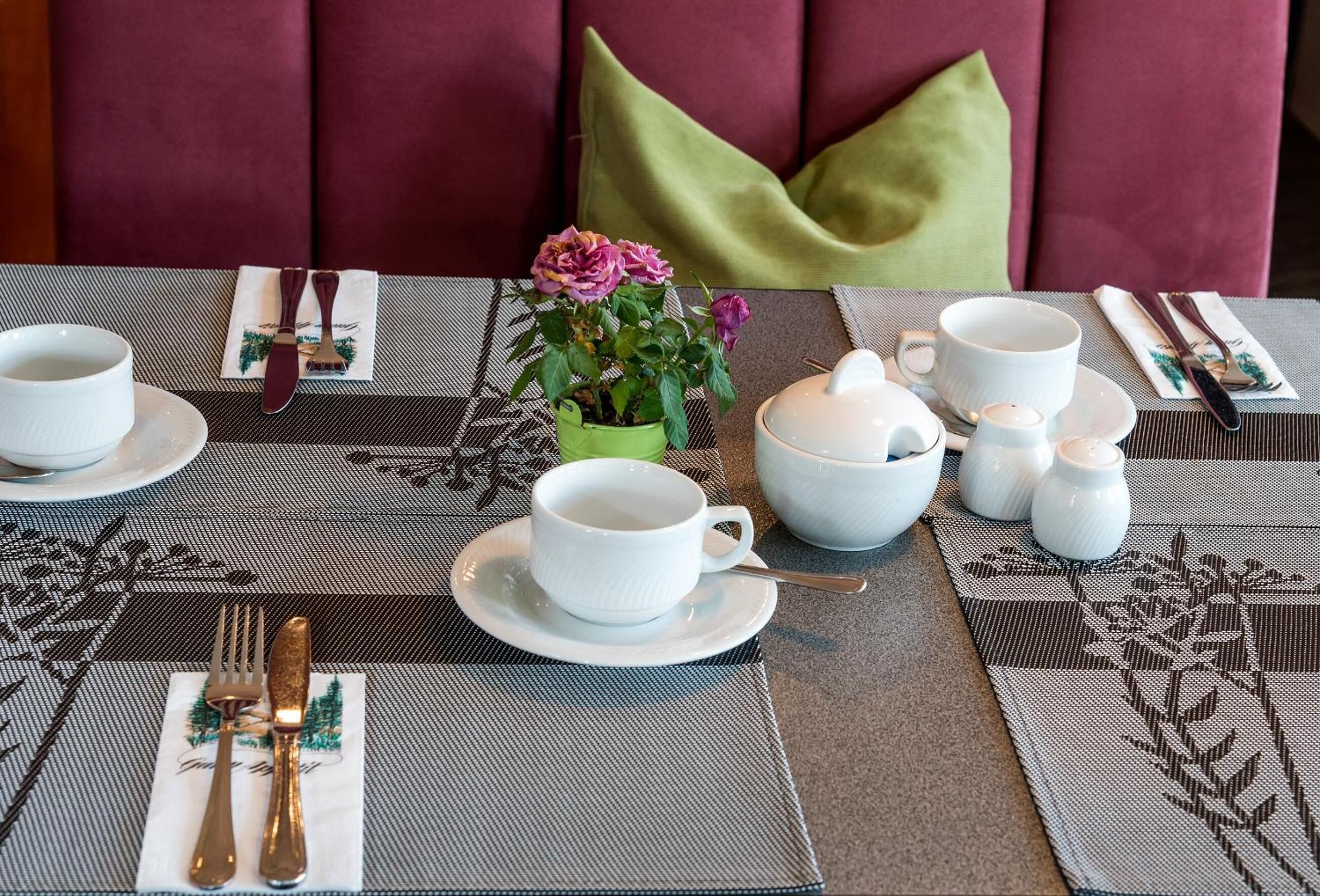 Una mesa de comedor dispuesta con tazas, platillos y un jarrón verde con flores.