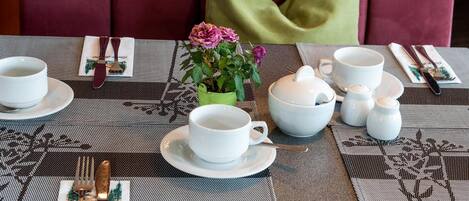 Una mesa de comedor dispuesta con tazas, platillos y un jarrón verde con flores.