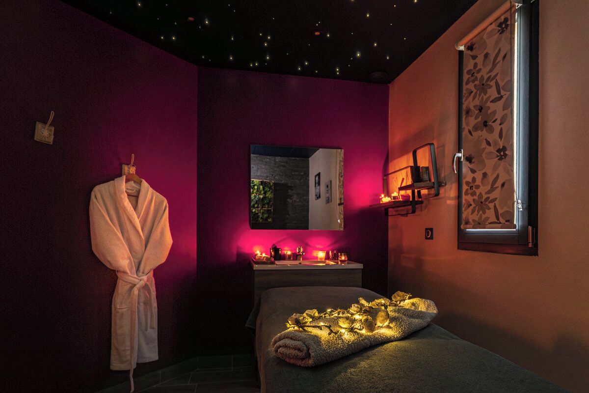 Habitación de spa con cama, una bata colgada en la pared, espejo y ventana con estampado floral.