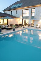 Una piscina con cubierta de madera, mobiliario exterior y un edificio con ventanas grandes y techo inclinado.