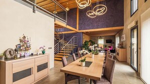 A spacious dining area with a long wooden table, comfortable seating, and modern pendant lighting. - Ome Sweet Home (Laubressel)