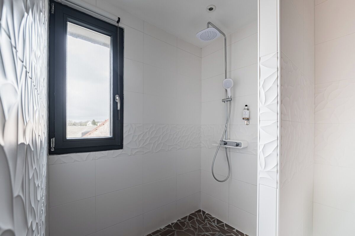 Eine Dusche mit Fenster, weißen Fliesen und einem gemusterten Boden.