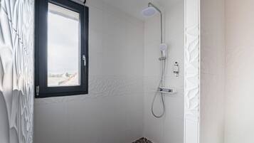 Eine Dusche mit Fenster, weißen Fliesen und einem gemusterten Boden.
