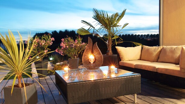 An outdoor seating area with a glass-top table, potted plants, and a sofa. - Ome Sweet Home (Laubressel)