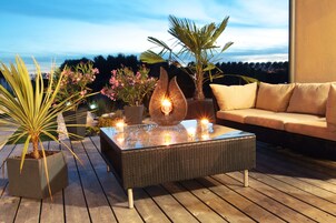 Un espacio al aire libre con una mesa de vidrio, plantas en macetas y un sofá.