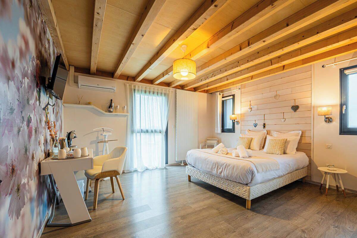 A bedroom with a bed, a desk, and a chair. There is a window with curtains, a wall-mounted air conditioner, and a wooden ceiling.