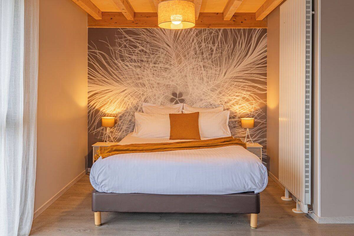 A bedroom with a bed, bedside lamps, a radiator, and a wooden ceiling.