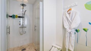 A modern bathroom with a glass shower enclosure, a white bath mat, and a white bathrobe hanging on the wall.