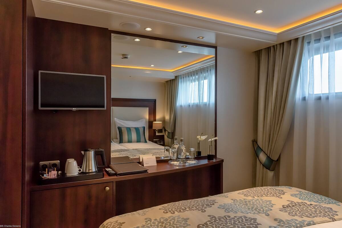 Habitación de hotel con una cama grande, una mesita de noche con cafetera, un televisor montado en la pared y un espejo grande que refleja la habitación.
