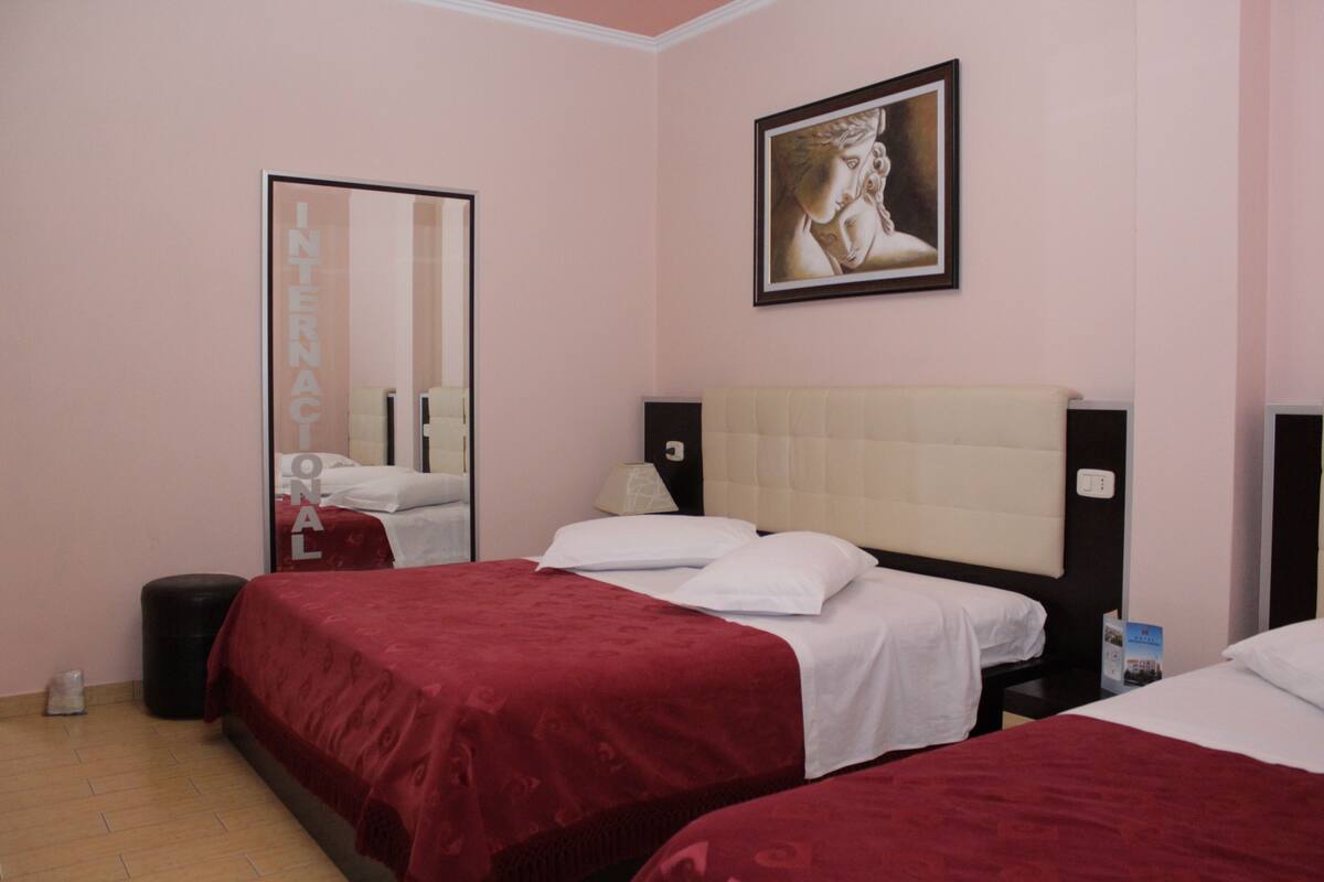 A hotel room with two beds, a large mirror, a framed artwork on the wall, and a small trash bin.