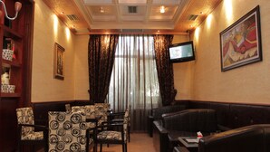 A hotel lobby with a seating area, a television mounted on the wall, and a large window with curtains. - Hotel International (Fier)