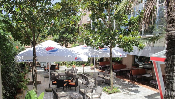 An outdoor seating area with tables and chairs, surrounded by greenery and umbrellas. - Hotel International (Fier)