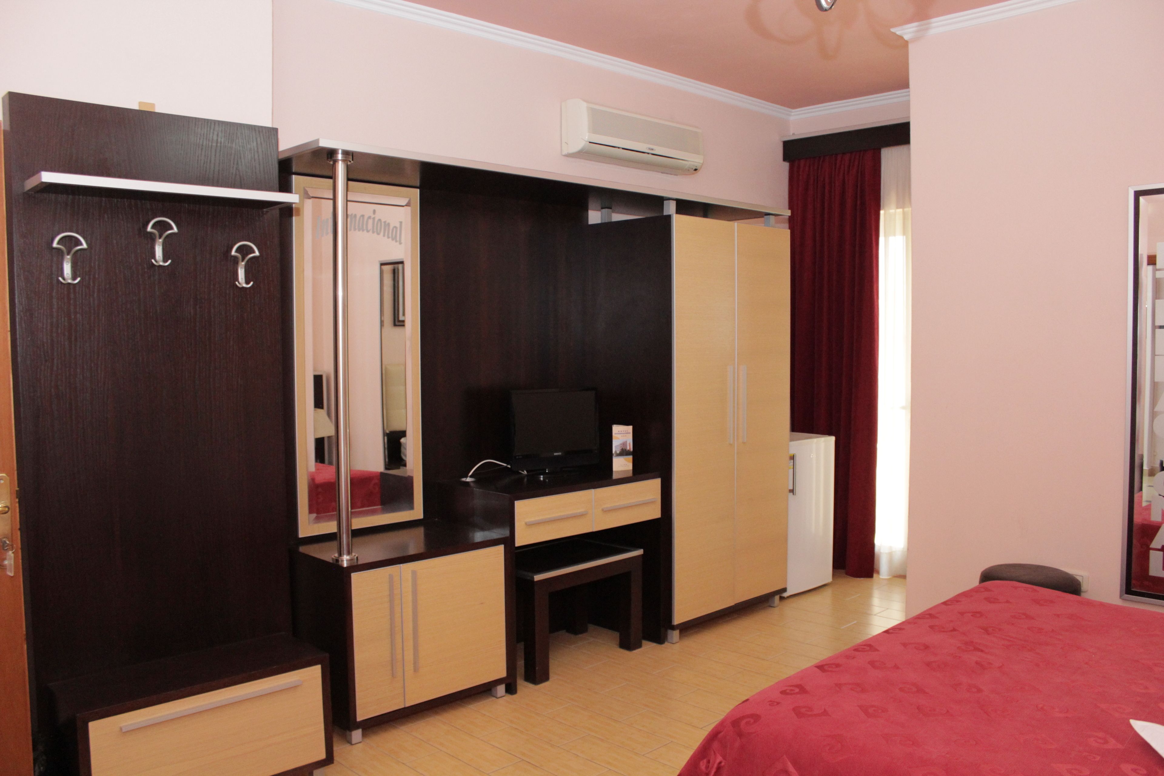 A hotel room with a bed, a desk with a chair, a wardrobe, a mirror, and a television.
