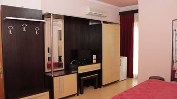 A hotel room with a bed, a desk with a chair, a wardrobe, a mirror, and a television.