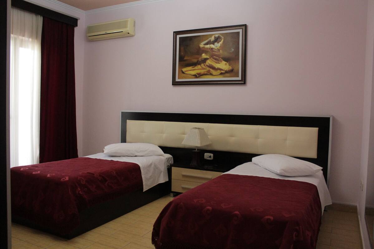 A hotel room with two beds, a painting on the wall, and an air conditioning unit.