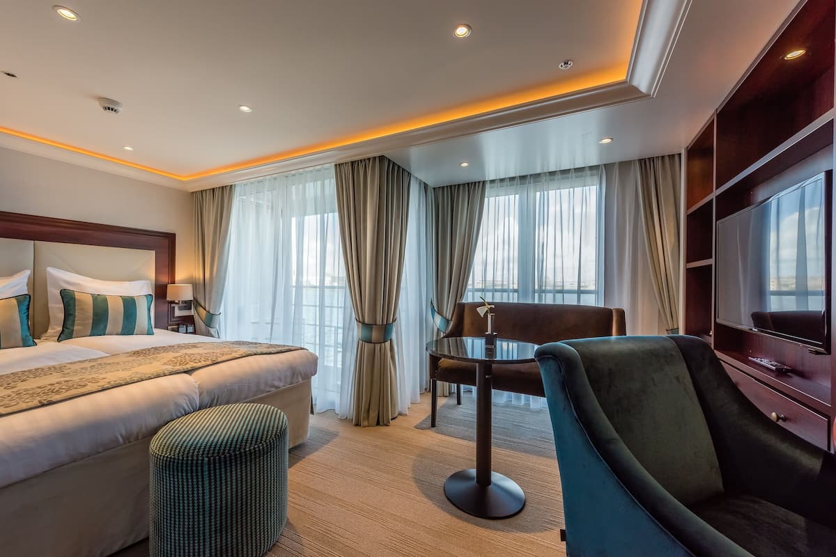 Quarto de hotel com uma cama grande, uma mesinha redonda, uma cadeira e uma televisão.