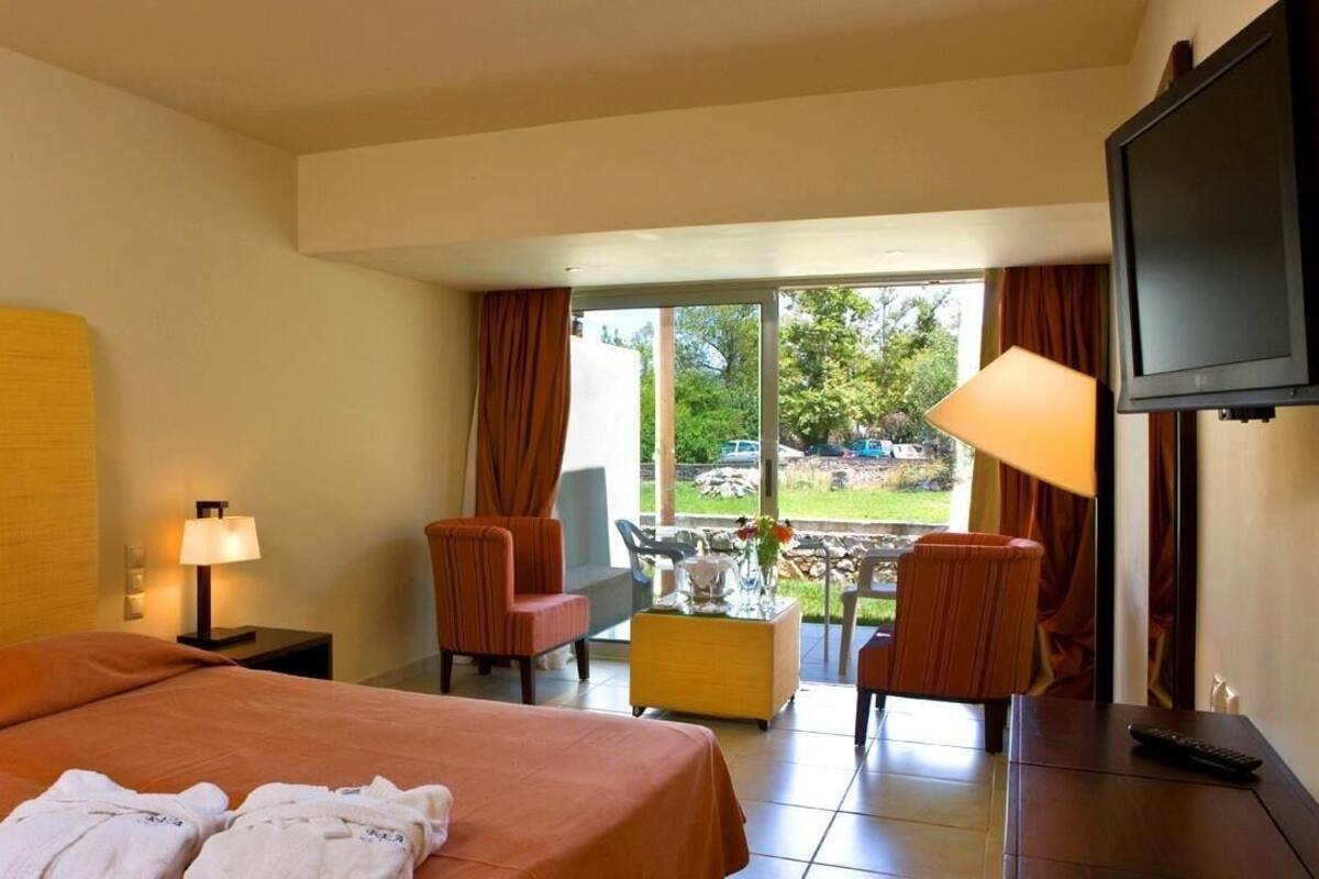 Quarto de hotel com cama, escrivaninha, cadeira, televisão e vista para o exterior.