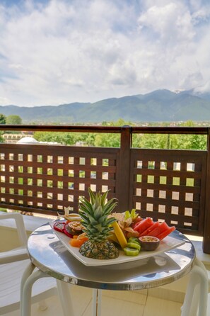 Een tafel met een fruitplateau op een balkon met uitzicht op bergen.