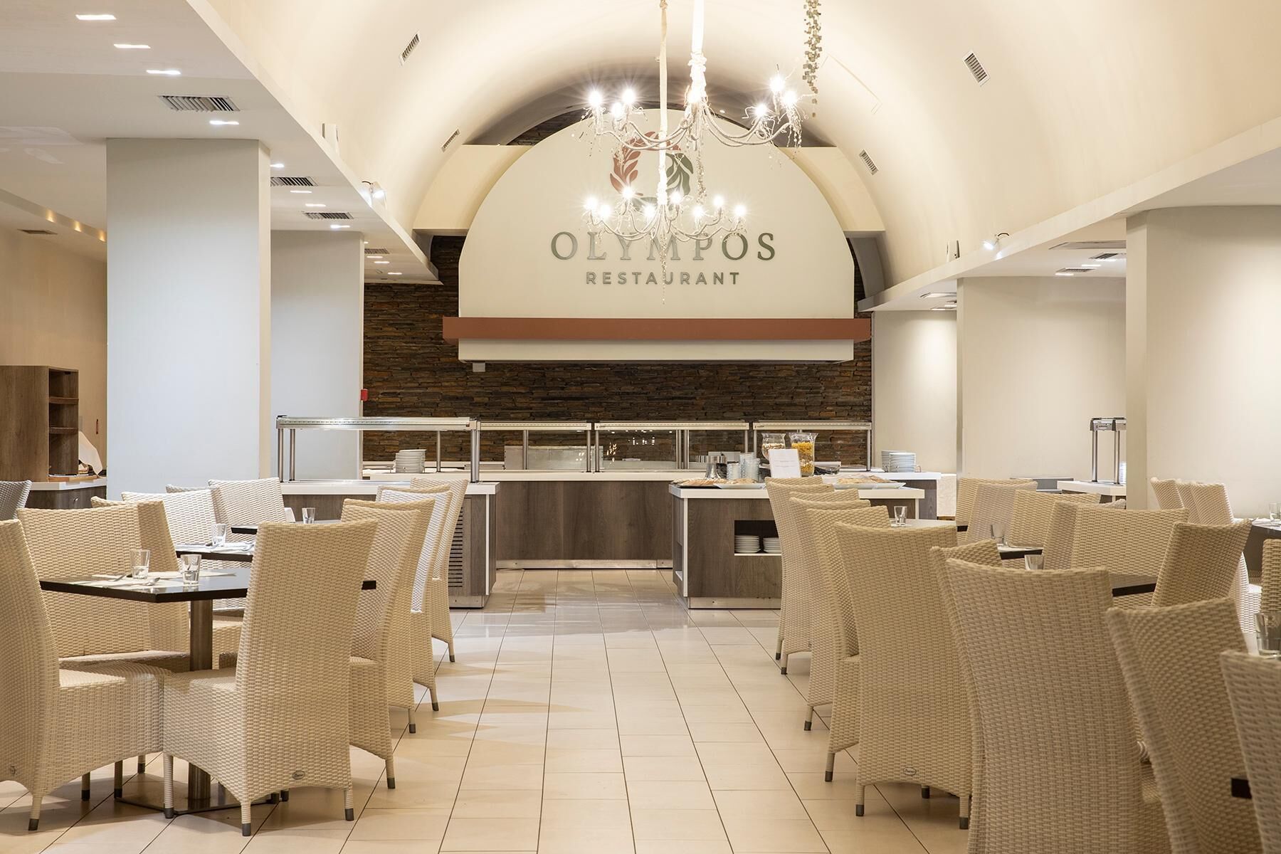 A restaurant interior with wicker furniture, a central kitchen area, and a chandelier.