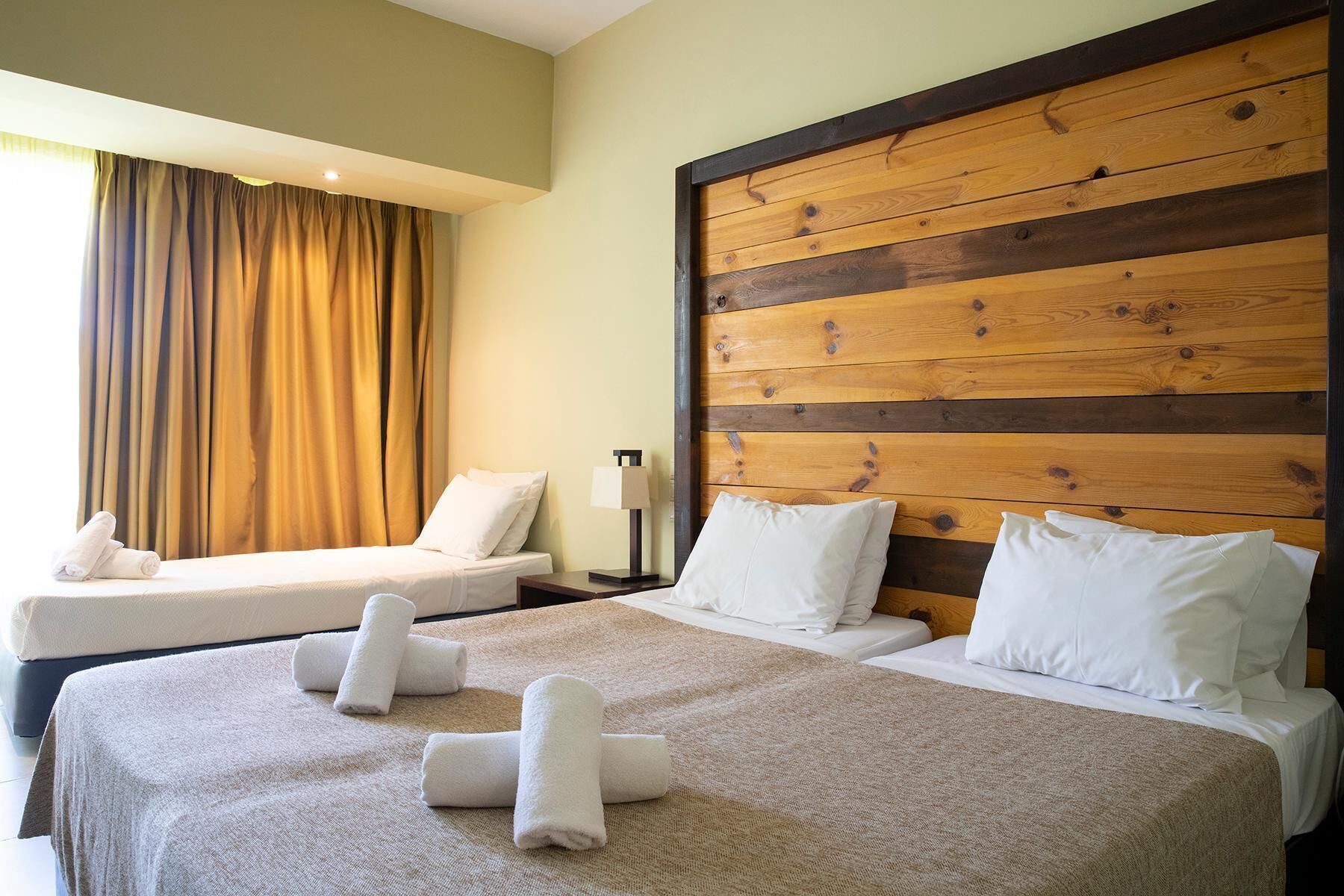 Una habitación de hotel con dos camas, un cabecero de madera y un amplio ventanal con cortinas.