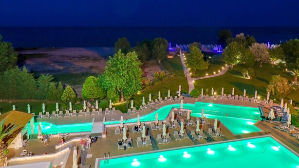 Une grande piscine extérieure avec plusieurs couloirs de nage, entourée de chaises longues et de parasols, et offrant une vue sur l’océan la nuit.
