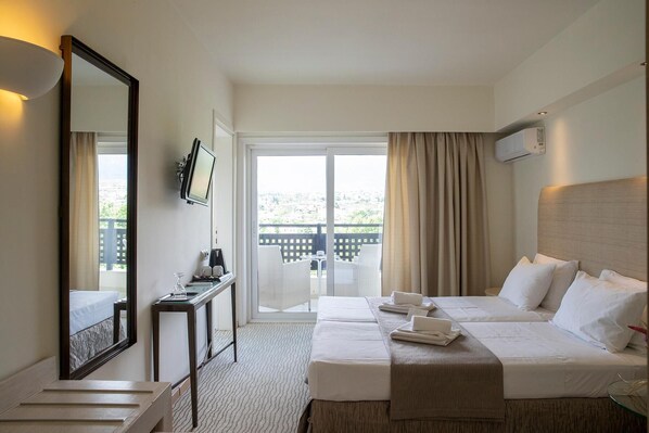 Een hotelkamer met een bed, een bureau met een computer, een televisie en een balkon met uitzicht.