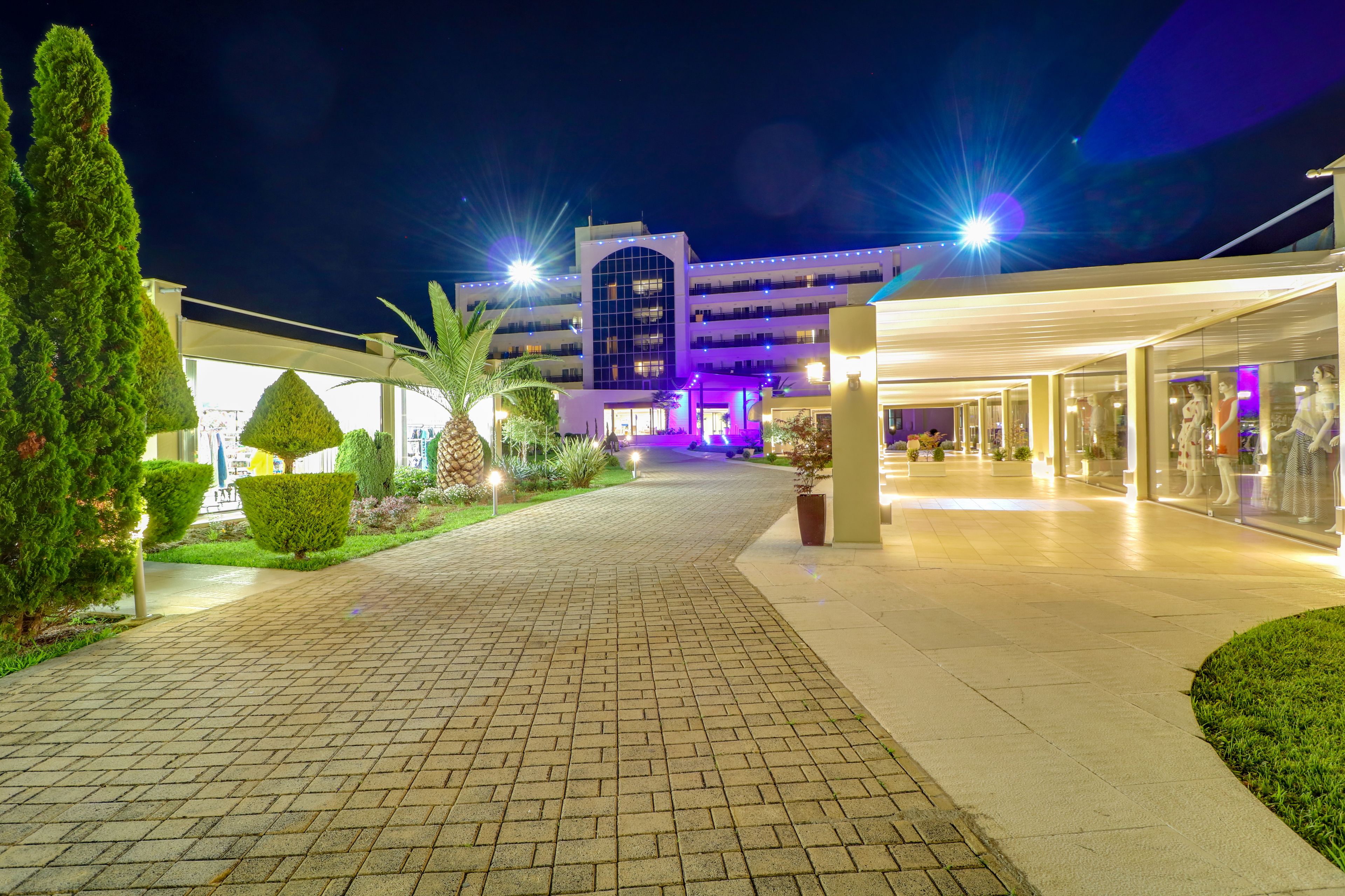 A hotel entrance with a paved walkway, well-lit exterior, and a building with multiple floors and balconies.