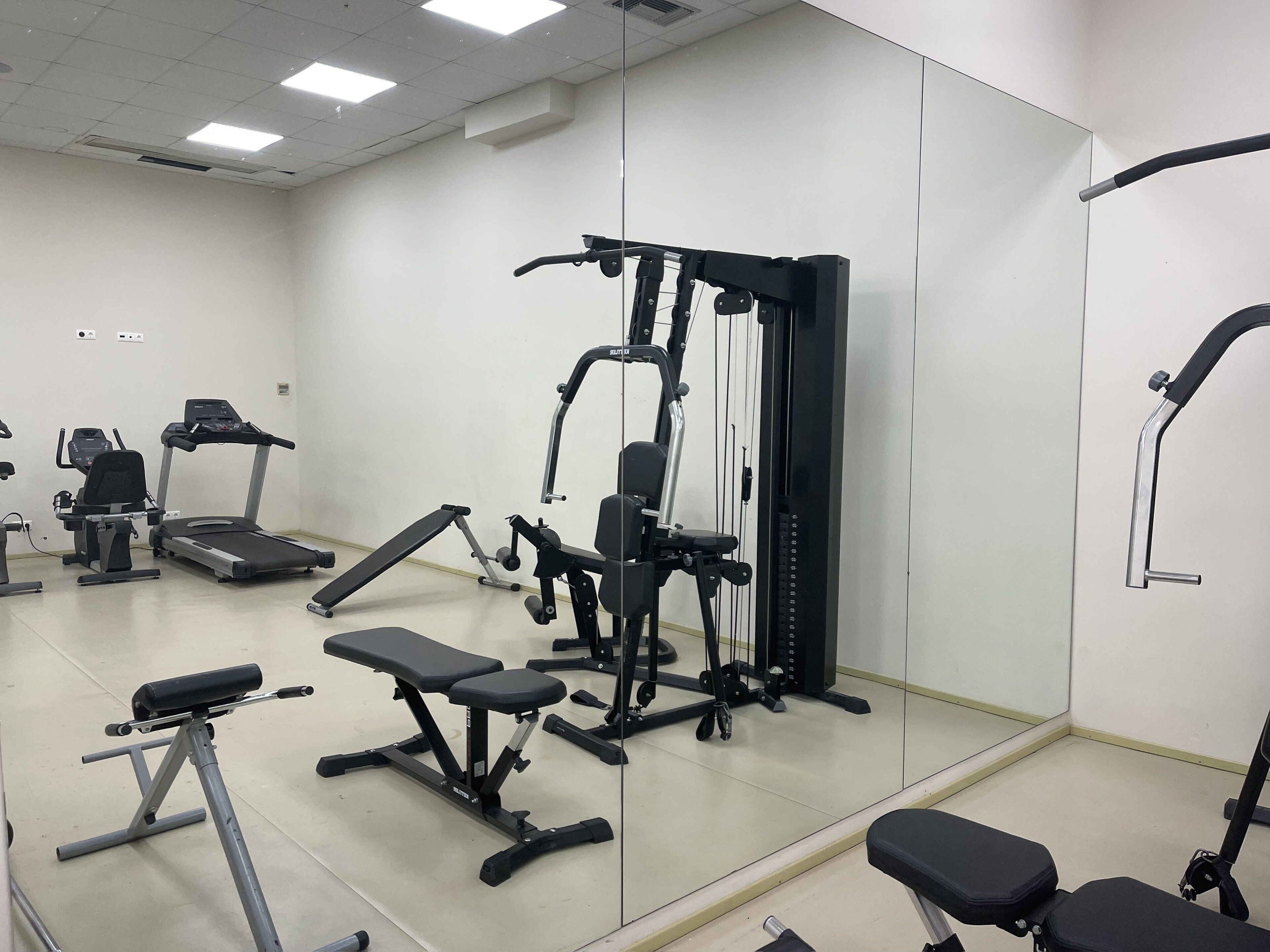 Une salle de sport équipée de divers appareils, notamment des tapis de course, des appareils de musculation et des bancs.