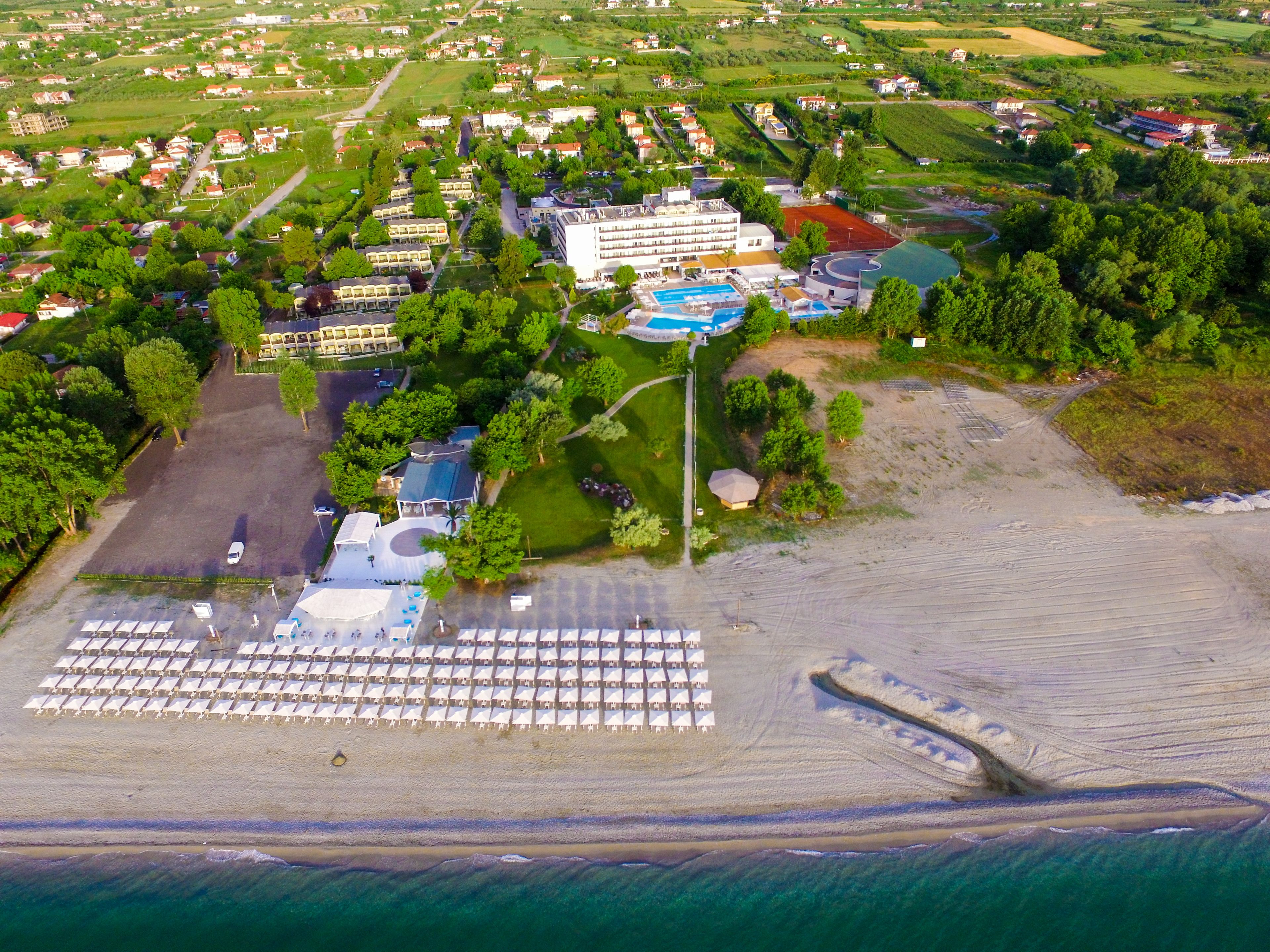 An aerial view of a coastal resort with a large pool area, multiple buildings, and a beach with umbrellas.