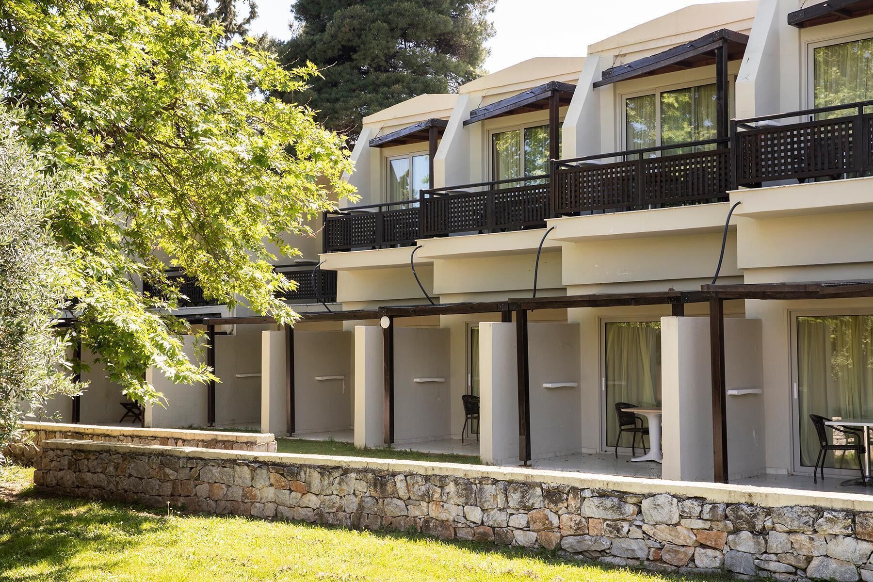 A modern building with a stone retaining wall, multiple balconies, and outdoor seating areas.
