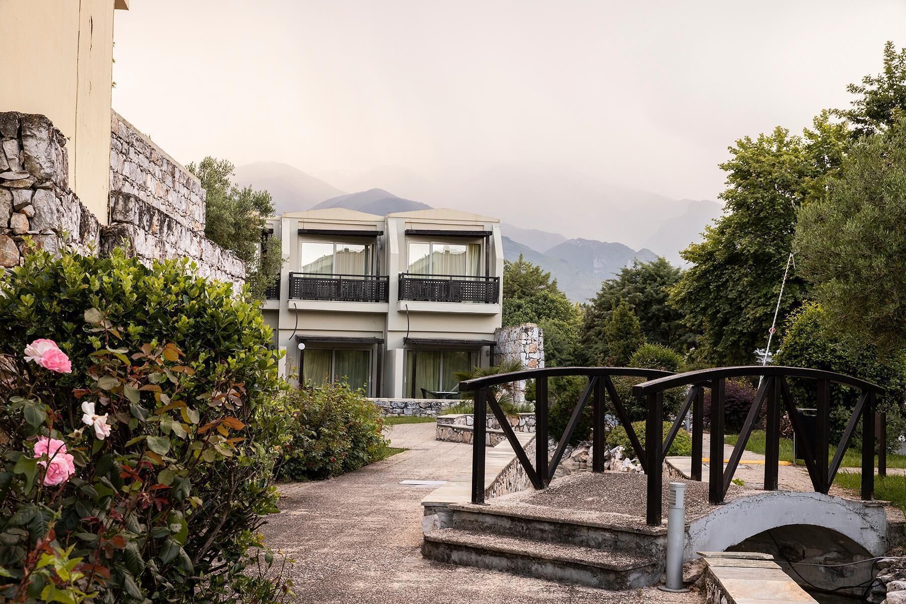 A two-story building with a balcony, surrounded by greenery and mountains in the background.