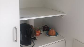 Eine Küchenzeile mit Kaffeemaschine, Wasserkocher und einigen Tassen auf der Arbeitsfläche.