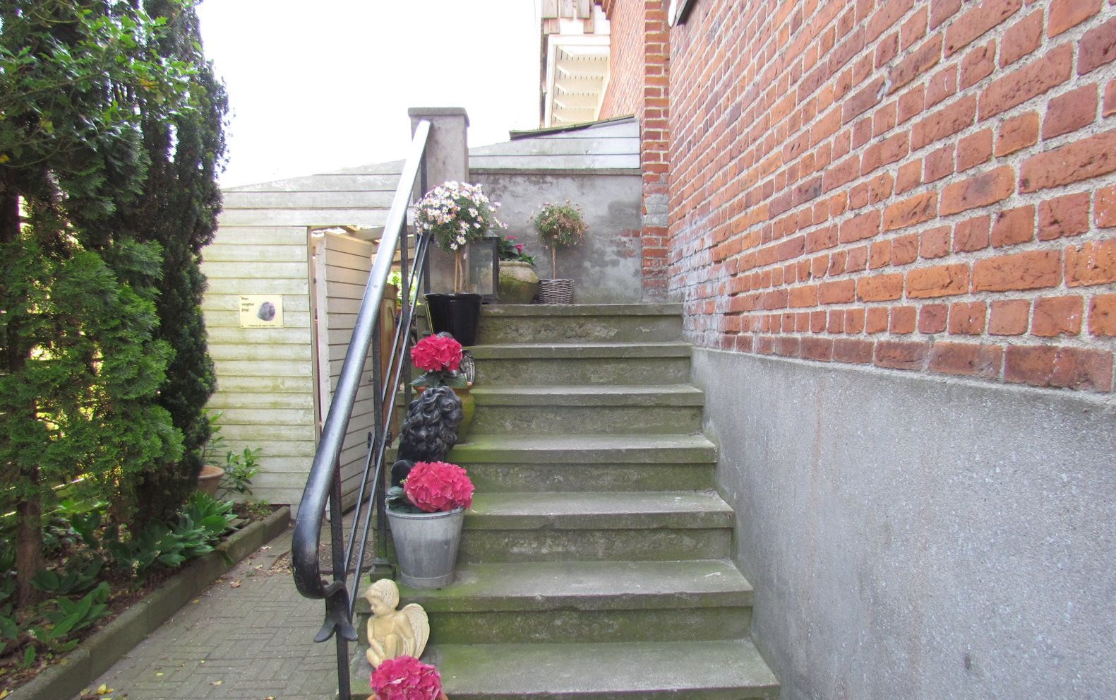 A set of concrete stairs with metal handrails, leading to a door. There are potted plants and flowers along the steps.