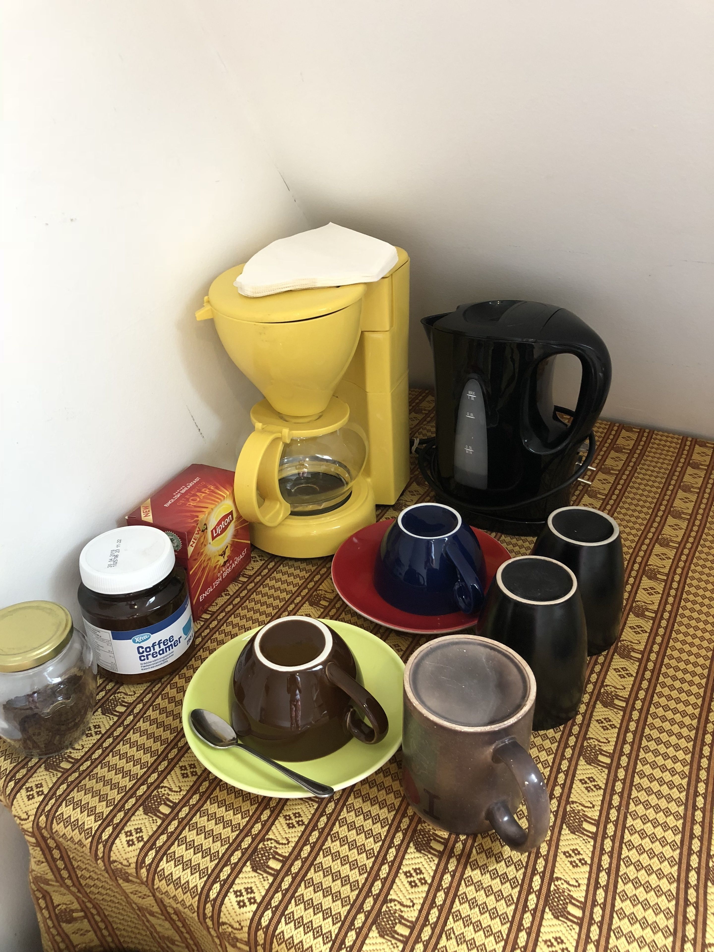 Una cafetera, un hervidor y varias tazas sobre un mantel estampado.