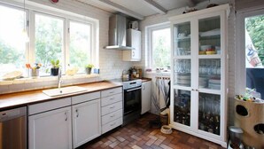 A kitchen with white cabinets, a wooden countertop, a built-in oven, and a window with a view of greenery. - Køge Bed & Kitchen (Koge)