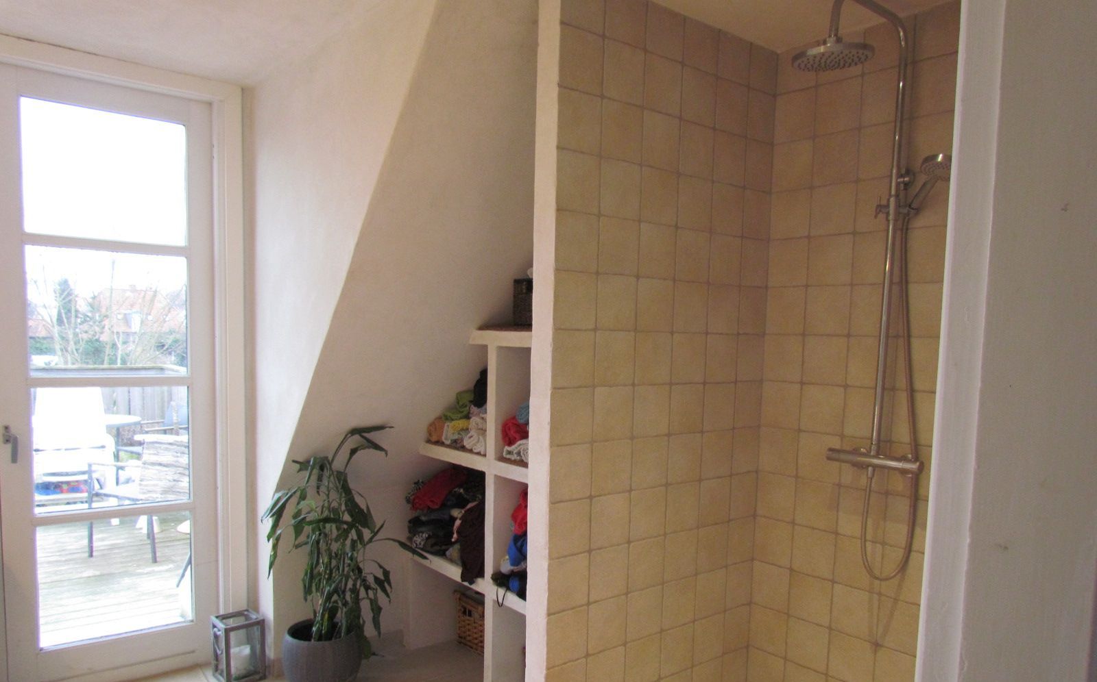 A bathroom with a shower, a potted plant, and a window.