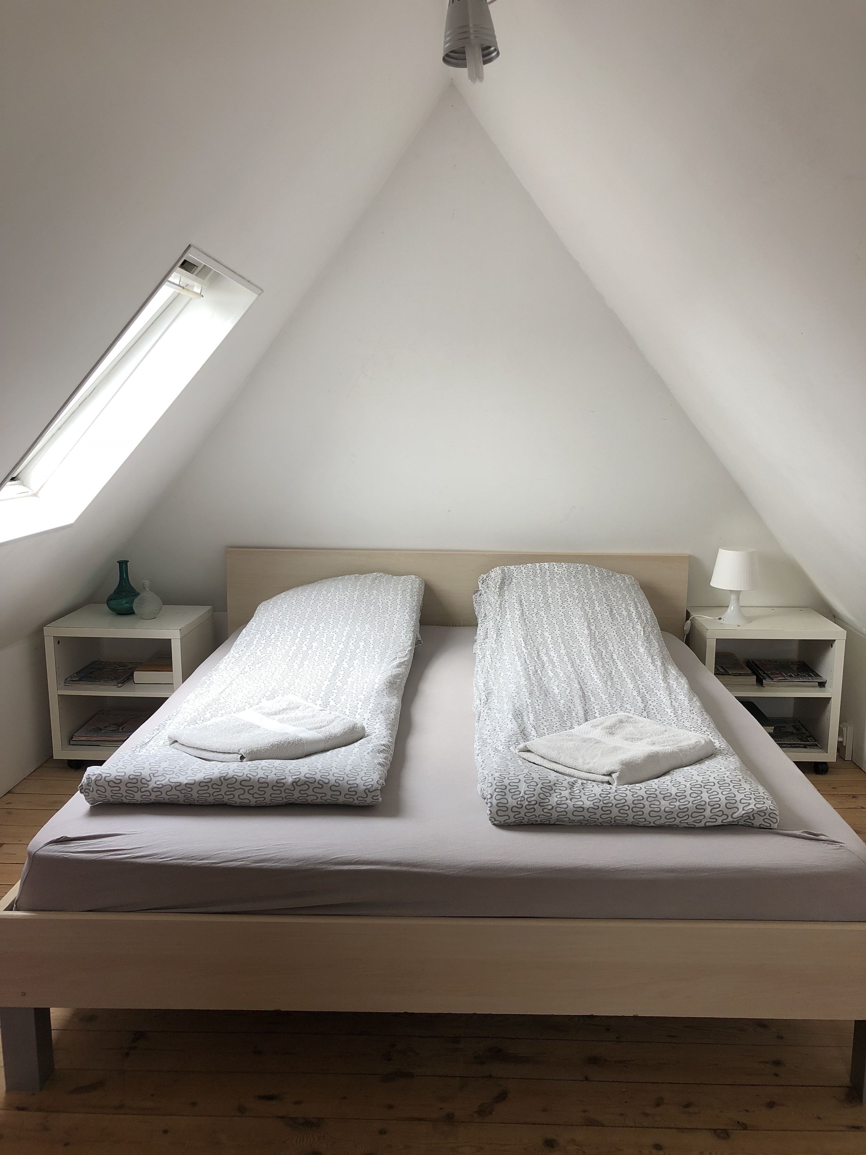 A bedroom with a sloped ceiling, two beds with patterned bedding, bedside tables with lamps, and a skylight.